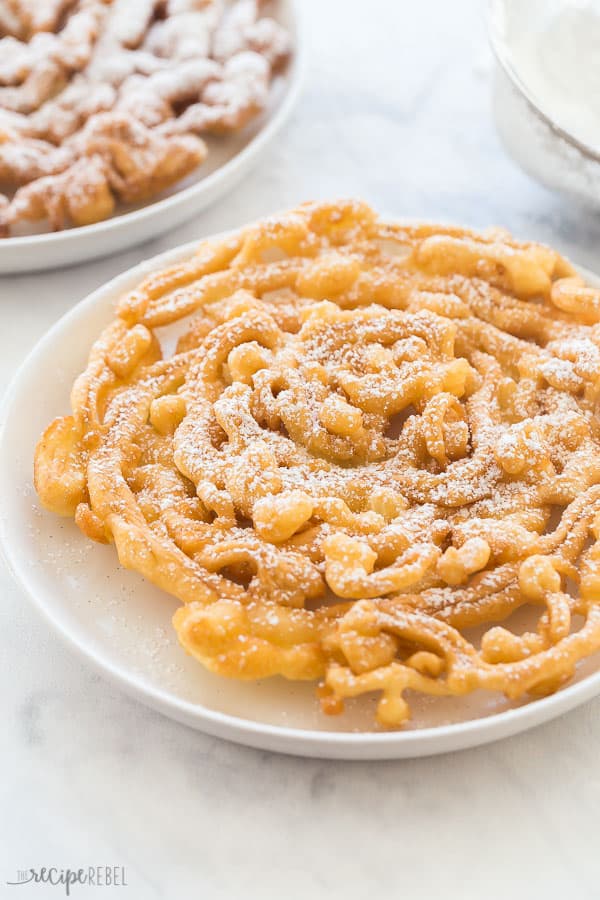 funnel cake on white plate on marble background with powdered sugar