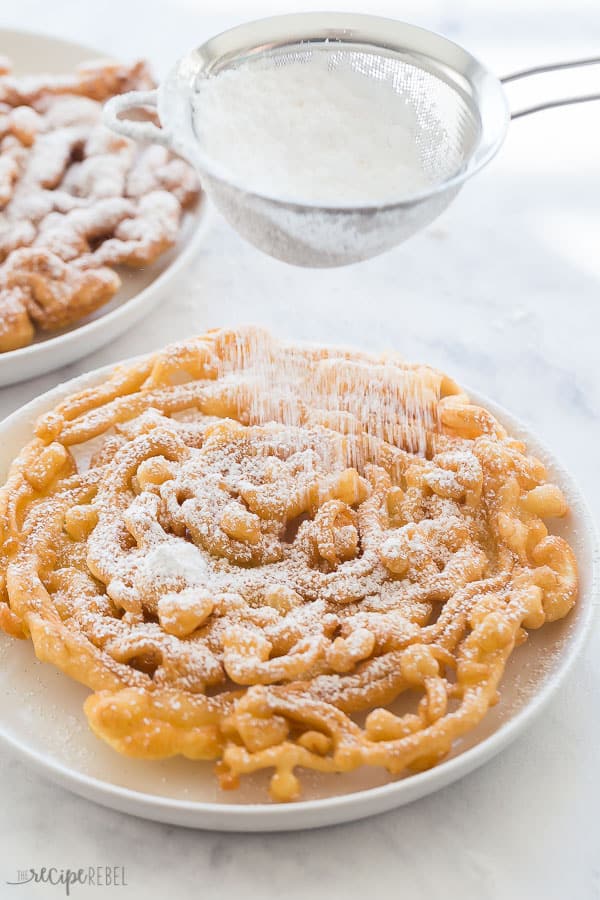 funnel cake with powdered sugar in sifter coming down