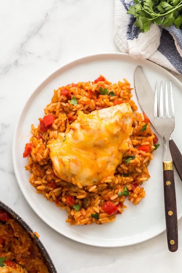 mango salsa chicken and rice on white plate on marble background with fork and knife