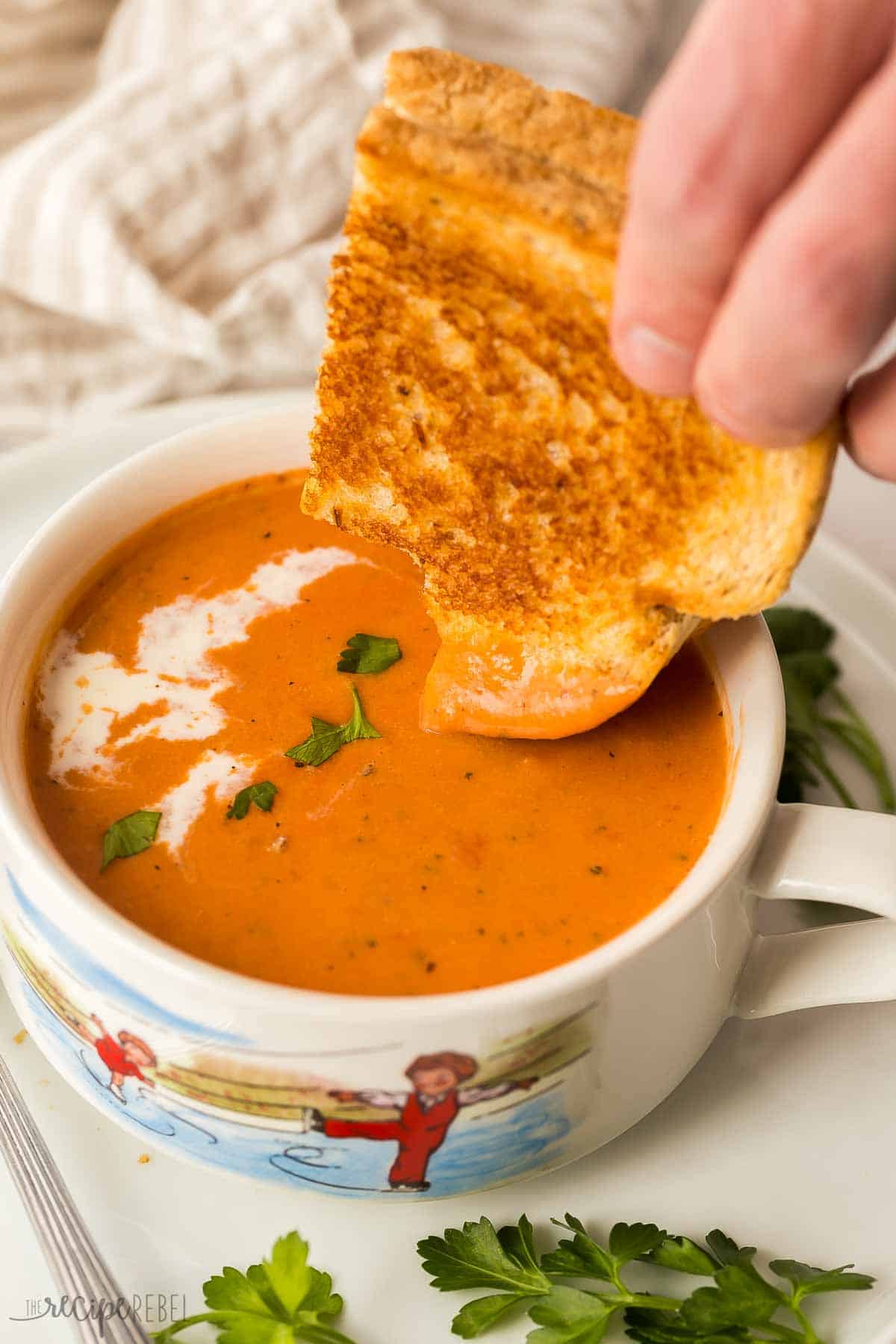 grilled cheese being dipped into a bowl of creamy tomato soup.