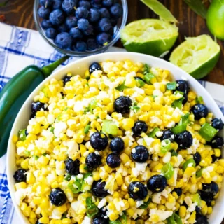 Top view of a large white bowl of blueberry, born and feta salad next to a smaller serving dish of blueberries and freshly squeezed limes.