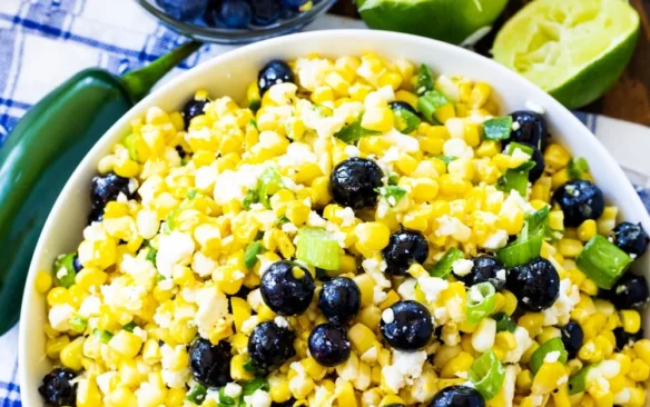 Top view of a large white bowl of blueberry, born and feta salad next to a smaller serving dish of blueberries and freshly squeezed limes.