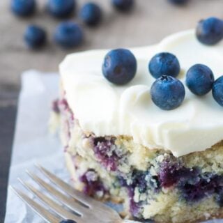 A slice of blueberry zucchini cake frosted with lemon buttercream and topped with fresh blueberries.