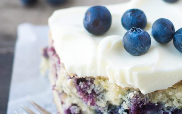 A slice of blueberry zucchini cake frosted with lemon buttercream and topped with fresh blueberries.