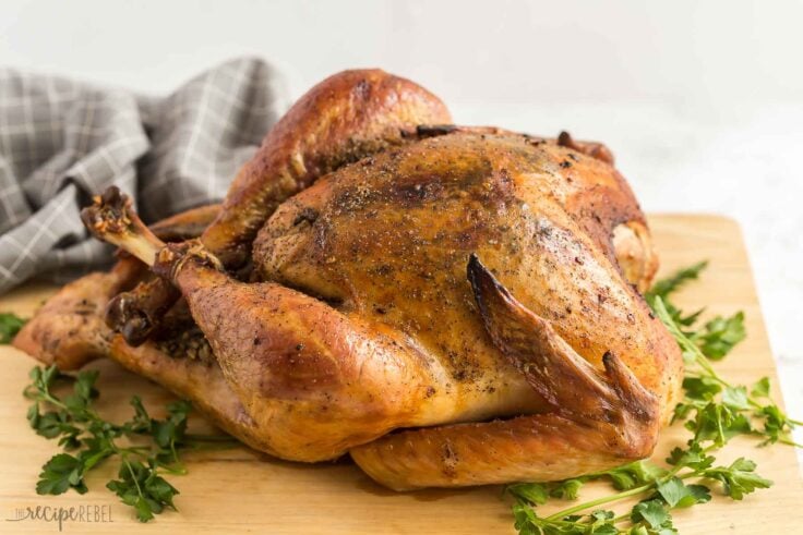 side image of whole roast turkey on cutting board with fresh parsley