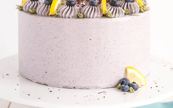 Frosted and decorated lemon blueberry cake on a cake stand.