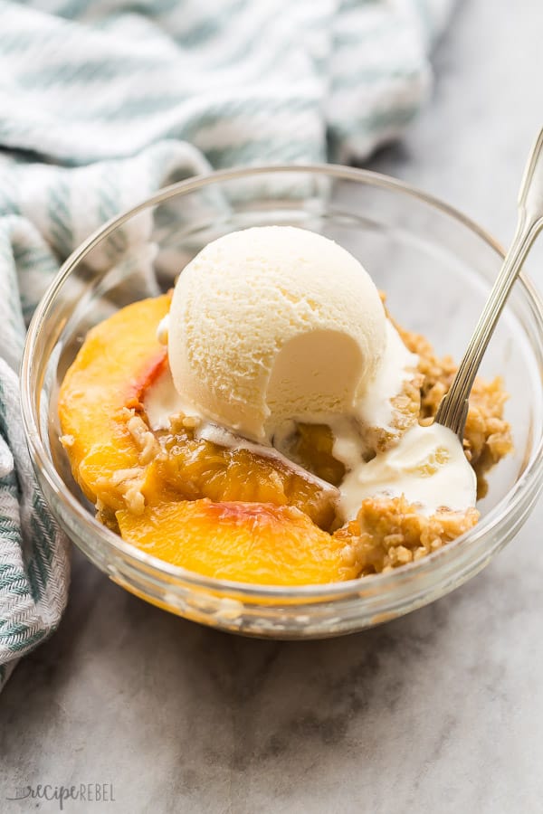 peach crisp with ice cream in bowl with blue towel in the background