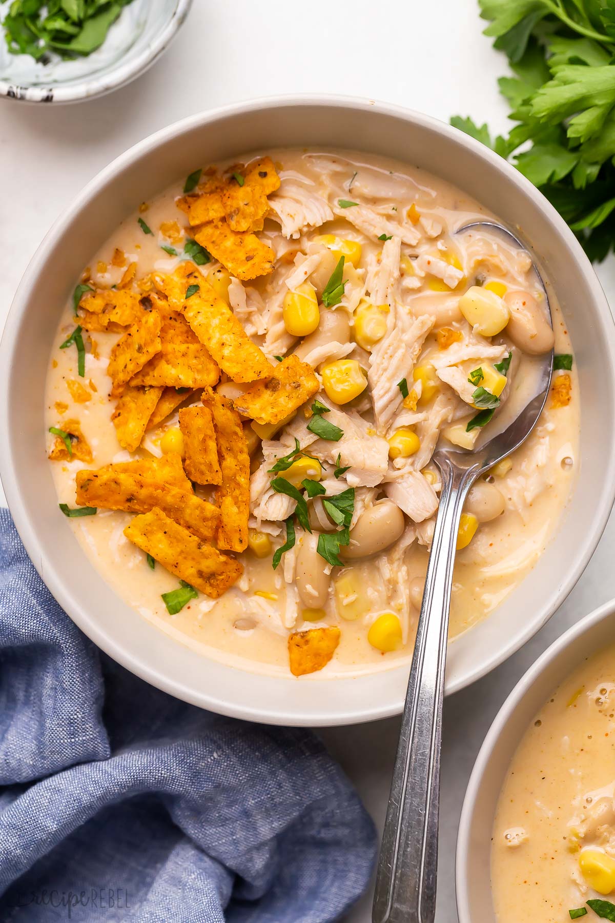 bowl of white chicken chili with spoon stuck in and tortilla strips on top.