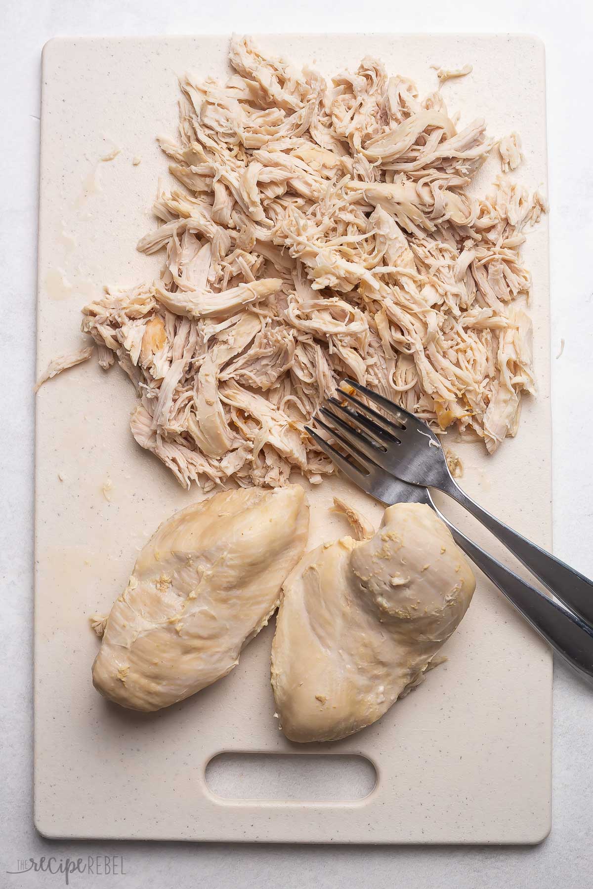 two forks shredding chicken breasts on a cutting board.