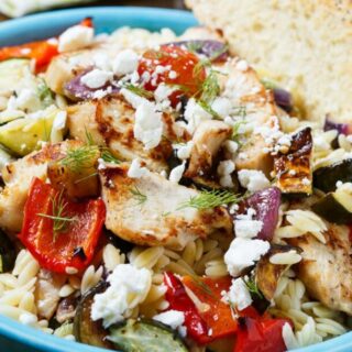 A blue bowl of orzo salad with chicken and roasted vegetables, served with a slice of bread.