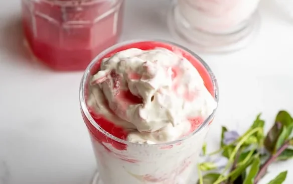 Two glasses of rhubarb fool side by side, topped with swirls of cream.