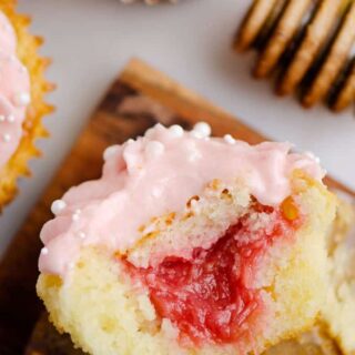 One half of a rhubarb cupcake showing the rhubarb filling, surrounded by other frosted cupcakes.