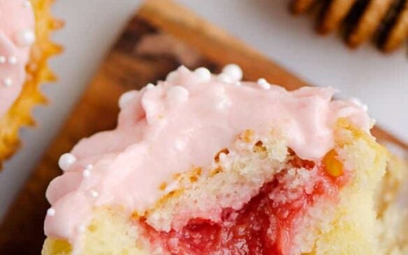 One half of a rhubarb cupcake showing the rhubarb filling, surrounded by other frosted cupcakes.