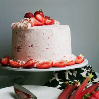 A whole rhubarb crisp cake topped with strawberries on a cake stand.