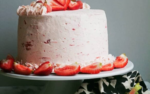 A whole rhubarb crisp cake topped with strawberries on a cake stand.