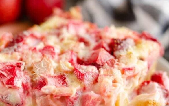 A slice of strawberry rhubarb custard dessert on a plate, with scattered strawberries in the background.