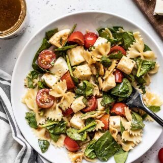 A large bowl of tomato mozzarella pasta salad with a serving spoon.