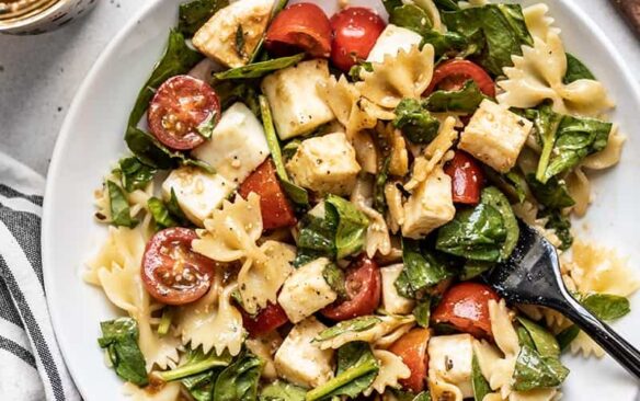 A large bowl of tomato mozzarella pasta salad with a serving spoon.