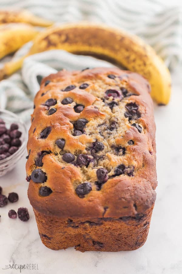 This Blueberry Banana Bread is ultra moist and fluffy, loaded with bananas and blueberries! Use fresh or frozen blueberries, and whole wheat or all purpose flour. #banana #blueberry #baking #bread #recipe blueberry banana bread whole loaf with bananas and blue towel on white background