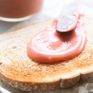 A piece of toast spread with rhubarb curd next to a jar of curd.