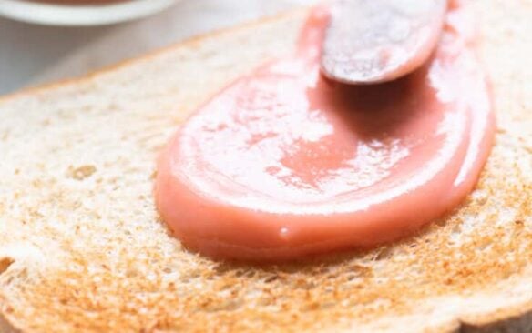 A piece of toast spread with rhubarb curd next to a jar of curd.