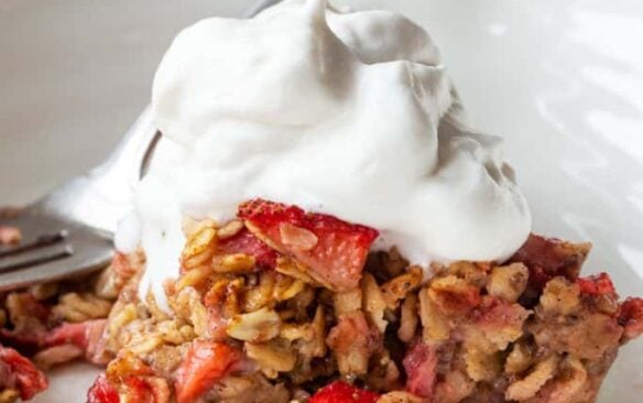 A serving of strawberry rhubarb oatmeal on a plate topped with whipped cream.