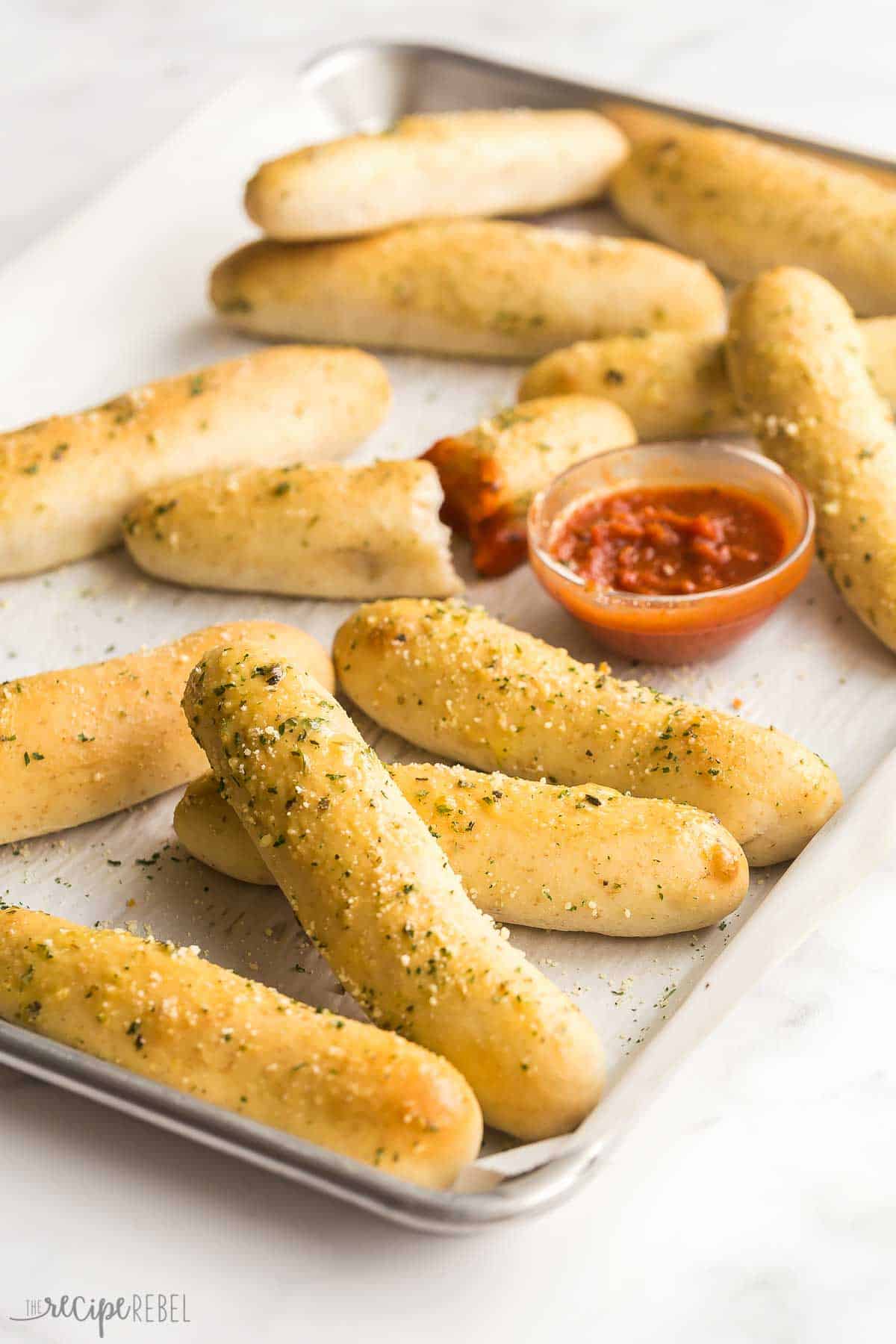 breadsticks on a sheet pan with a bowl of tomato sauce.
