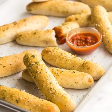 breadsticks scattered on sheet pan with tomato sauce
