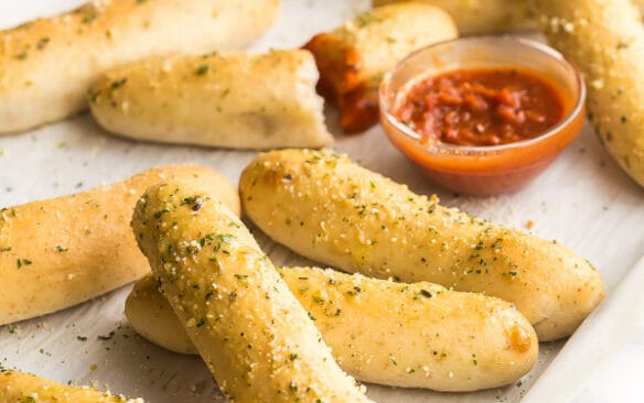 breadsticks scattered on sheet pan with tomato sauce