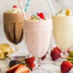 strawberry banana and chocolate milkshakes in glasses with straws.