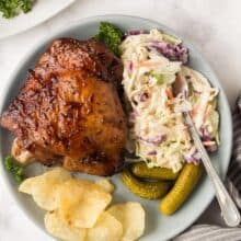 grilled turkey thighs on blue plate with coleslaw pickles and chips