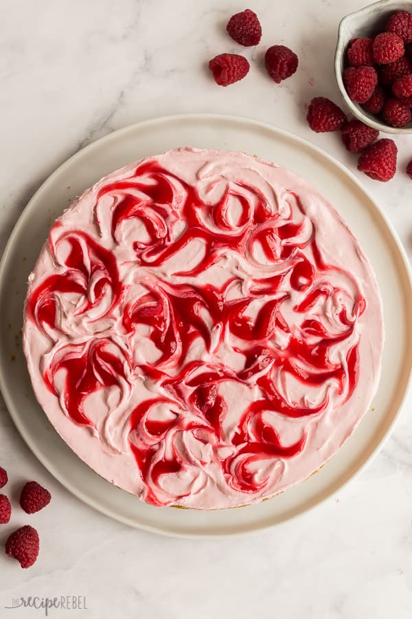 no bake raspberry cheesecake whole on white plate with fresh raspberries on the side