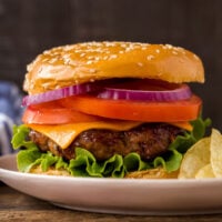 beef burger on bun with lettuce tomato and onion against black background