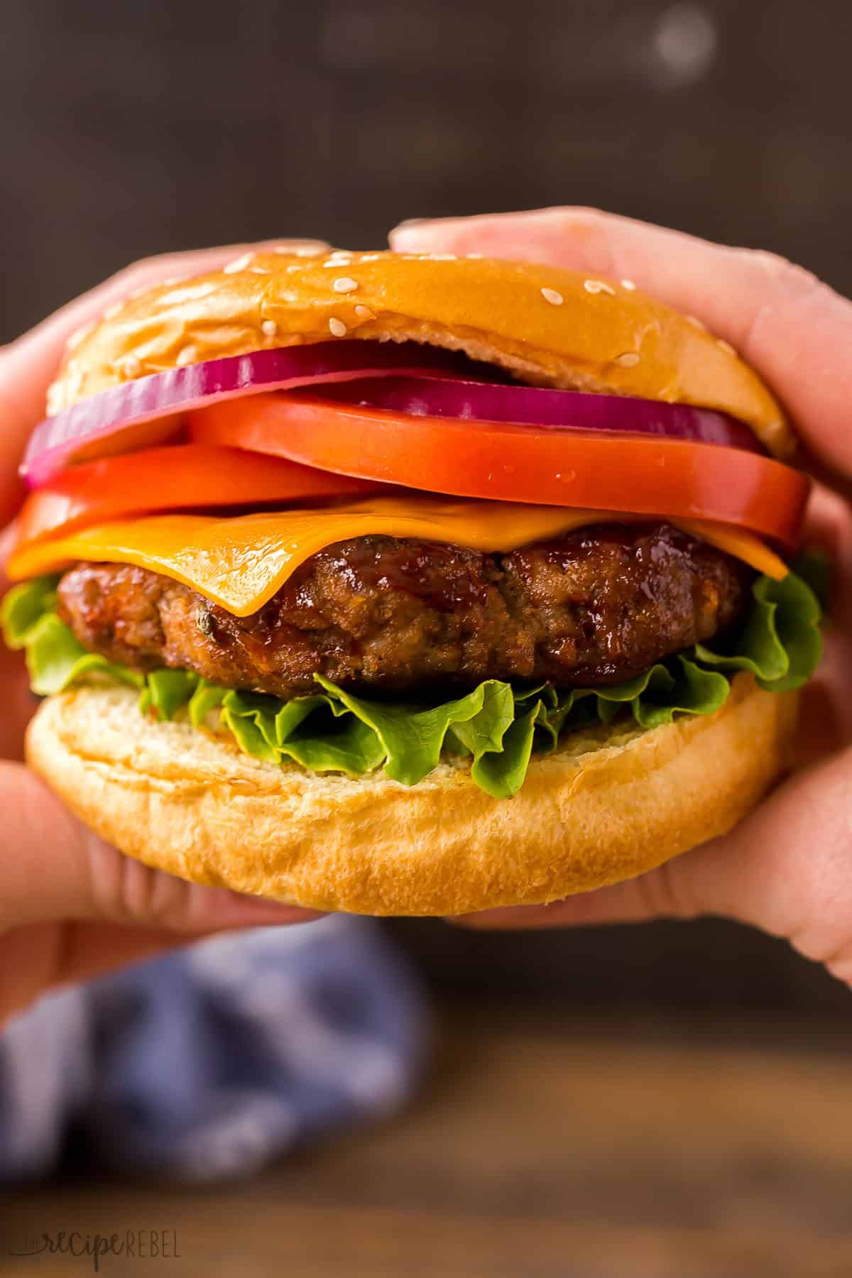 the best hamburger recipe on a bun with toppings held in hands.