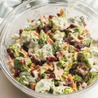 broccoli salad in glass bowl with cranberries cheese and bacon