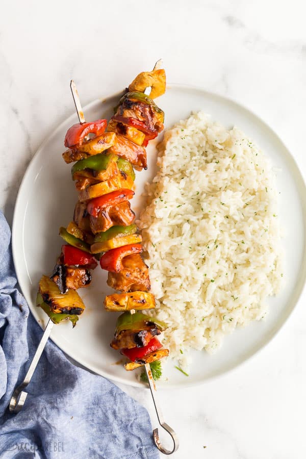 chicken kabobs on white plate with white rice and blue towel on the side