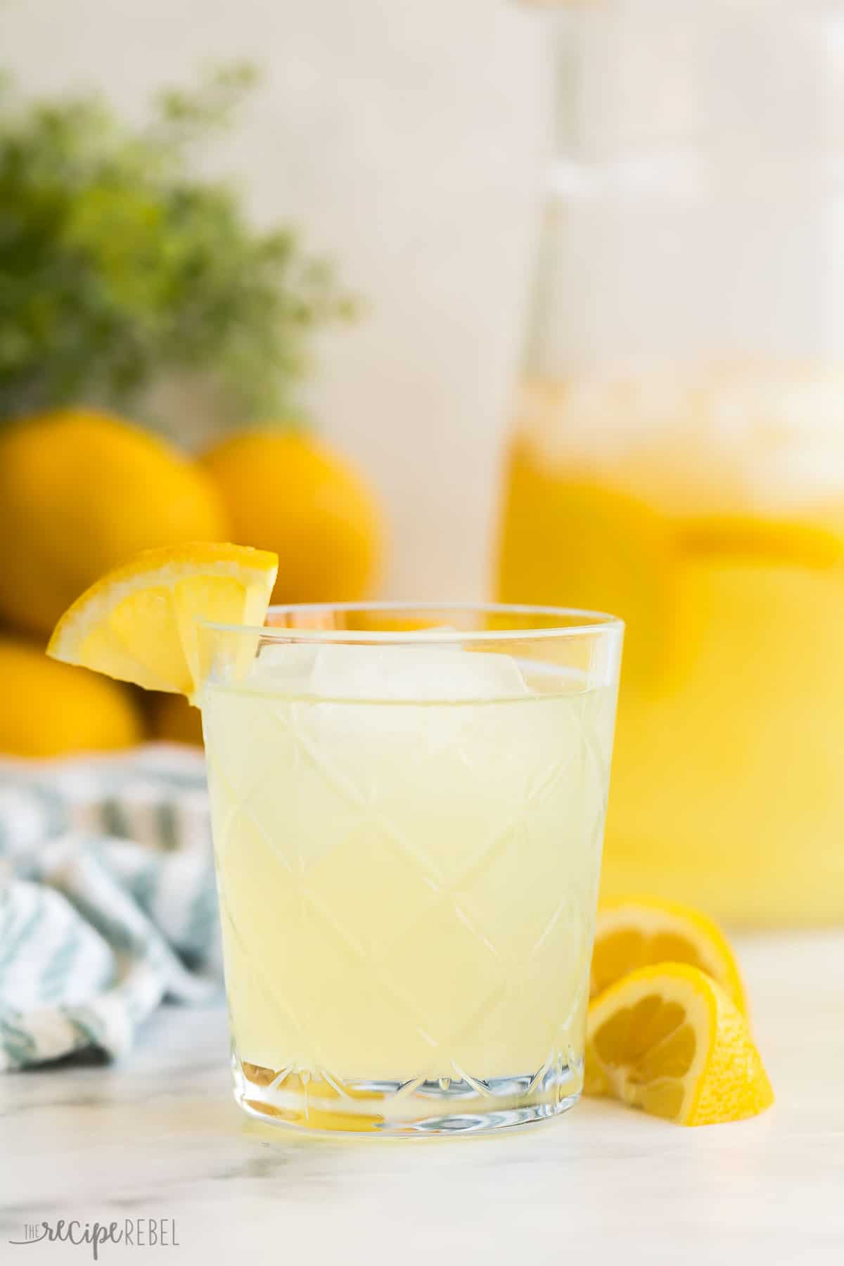 This easy homemade Lemonade recipe is perfect for summer! It's fresh and tangy, includes strawberry and blueberry variations, plus tips and creative uses for simple syrup. #lemonade #drink #recipe | lemonade recipes | lemon recipes | summer drinks | blueberry lemonade | strawberry lemonade | lemon recipes | easy drink recipes glass of homemade lemonade recipe with pitcher in the background.