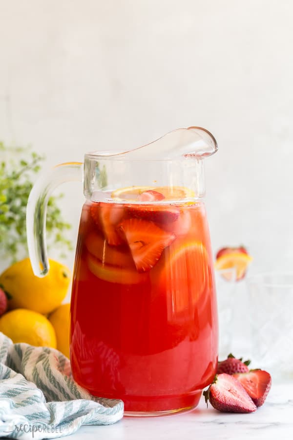 strawberry lemonade in large glass pitcher with lemon slices and strawberries