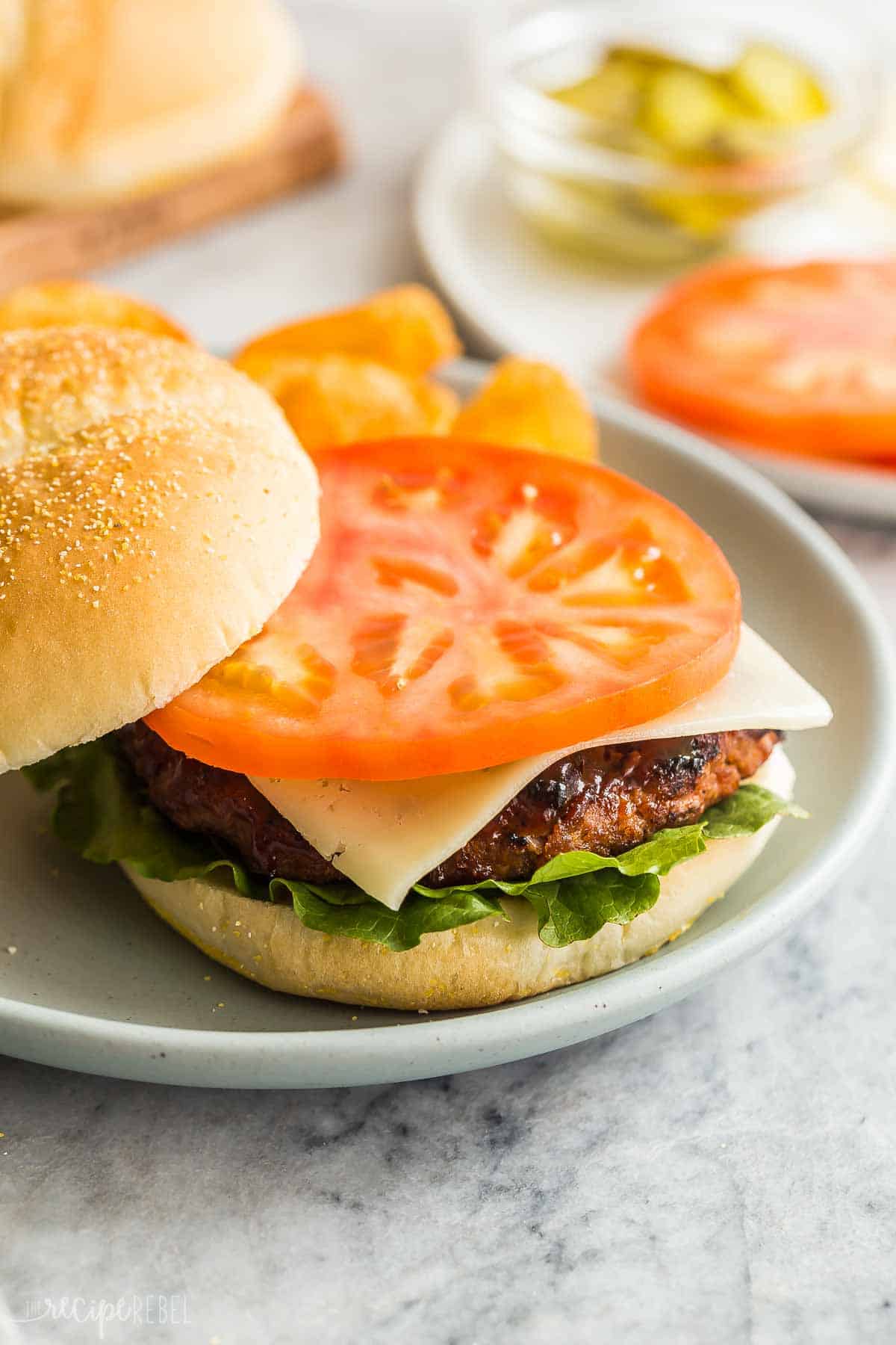 These Grilled Turkey Burgers are an easy summer meal that is make ahead and freezer friendly! The perfect healthy meal prep dinner for summer, and loaded with flavor from red onion and barbecue sauce! #dinner #recipe #burger | grilling recipes | summer food | summer dinner | burger recipes | turkey burger recipe | ground turkey | healthy burgers a bun on a plate with grilled turkey burger, tomato, lettuce and cheese.