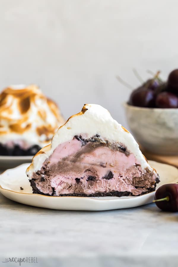 one baked alaska tart half on white plate with fresh dark cherries