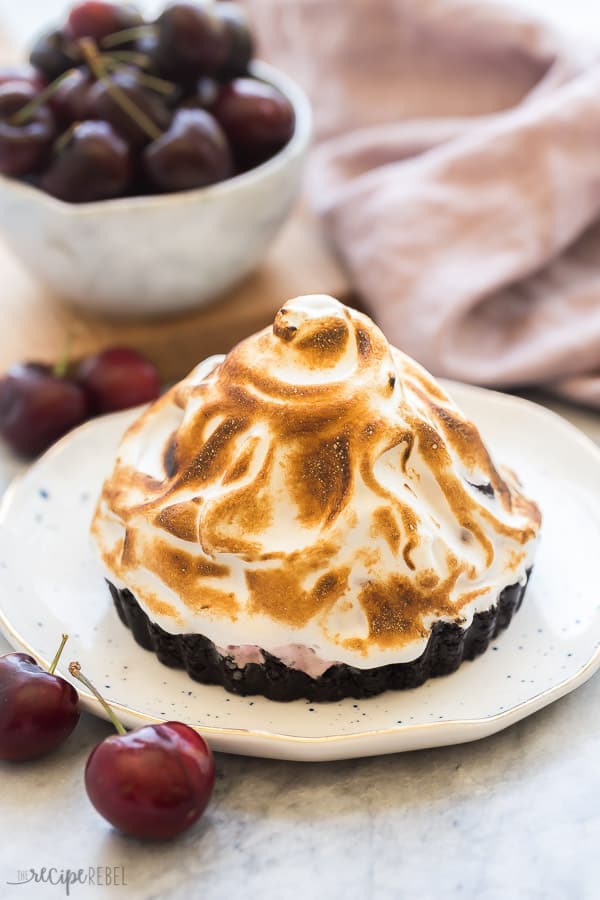 These Baked Alaska Tarts are a mini version of a classic Baked Alaska, made with a no bake cookie crust, filled with frozen yogurt and topped with toasted meringue! With step by step recipe video. #bakedalaska #icecream #dessert #recipe one baked alaska tart with toasted meringue on white plate