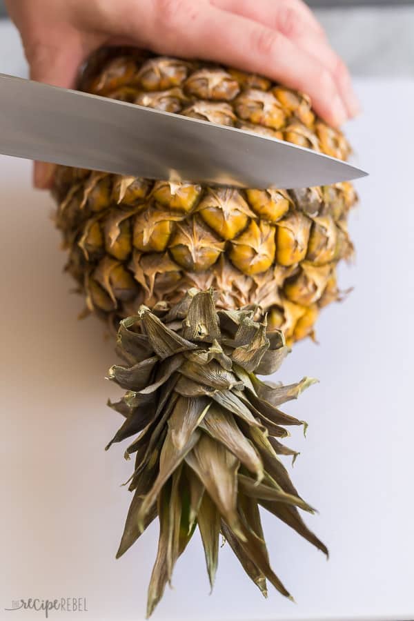 how to cut a pineapple first step cut off the top on white cutting board