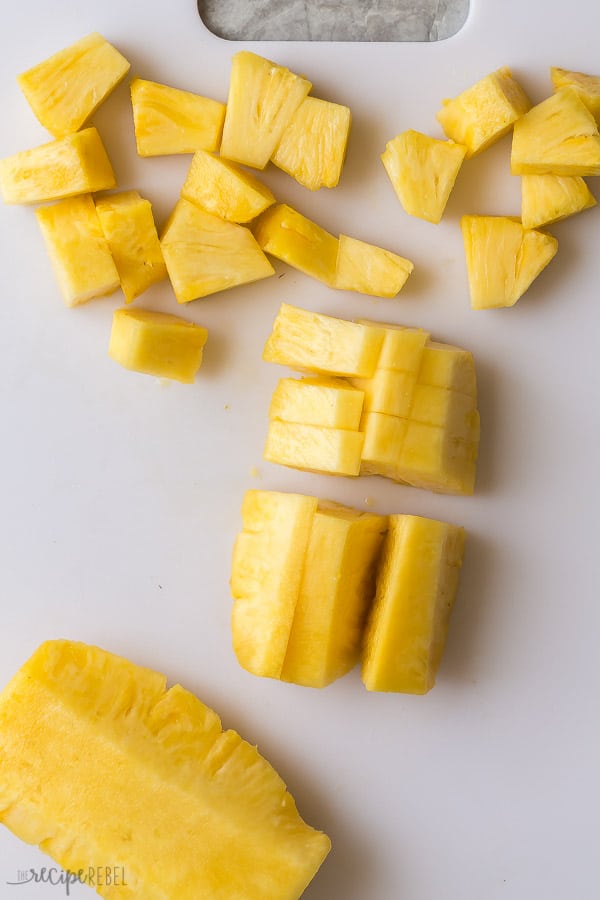 cutting a pineapple on a white cutting board with some pineapple spears and some pineapple chunks