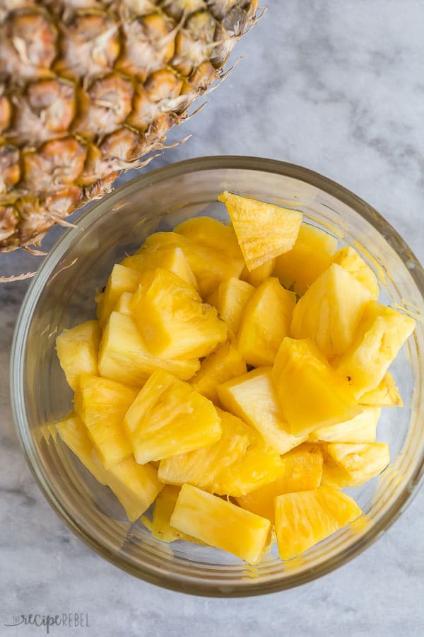 cut pineapple chunks in glass bowl with whole pineapple on the side