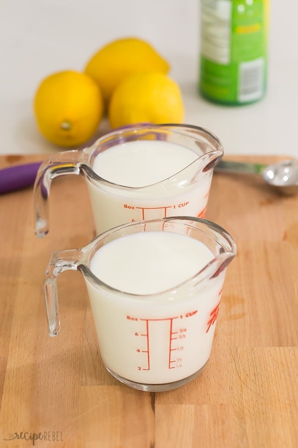 This easy buttermilk substitute requires just two ingredients and a few minutes! It adds so much flavor to pancakes, waffles and baked goods! #buttermilk #baking #recipe milk in two one cup measuring cups on a wooden cutting board with lemons and lemon juice in the background