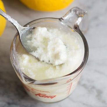curdled milk in one cup glass measuring cup with lemons in the background