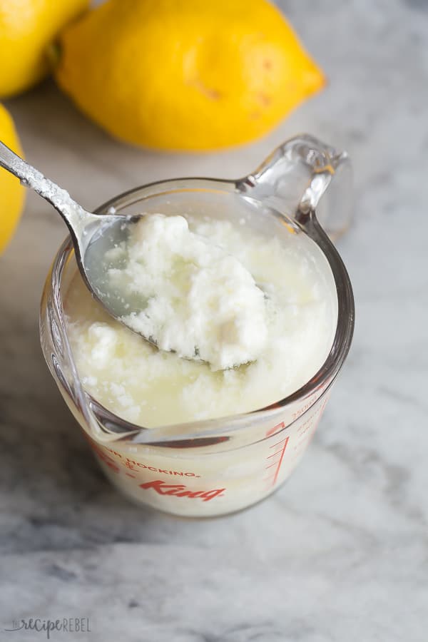 curdled milk in one cup glass measuring cup with lemons in the background