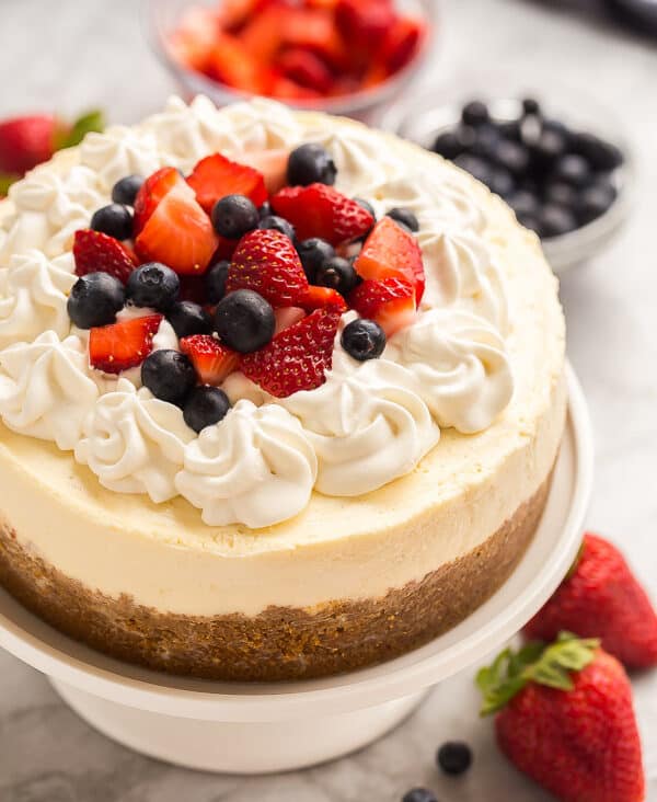 instant pot cheesecake on white cake plate with whipped cream strawberries and blueberries