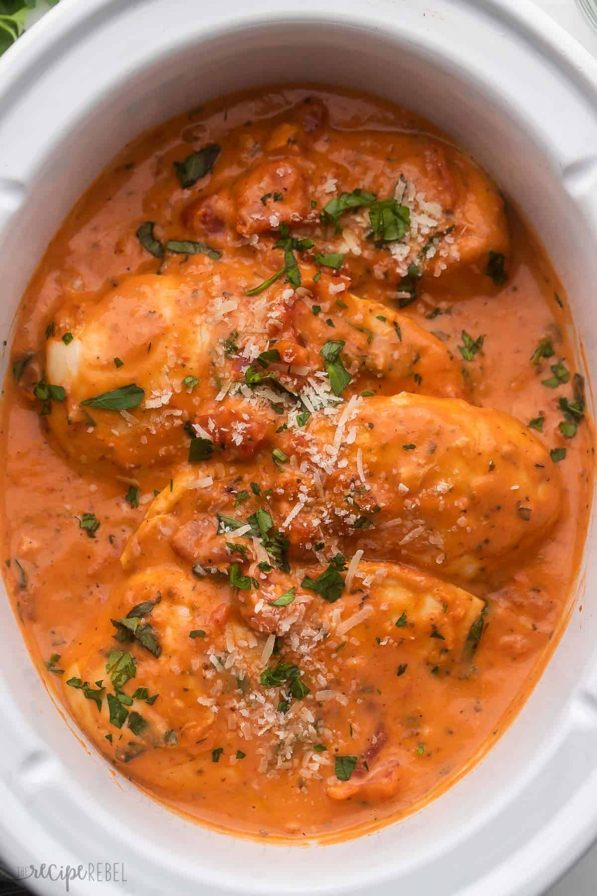 overhead image of slow cooker creamy tomato basil chicken breast in white crockpot.