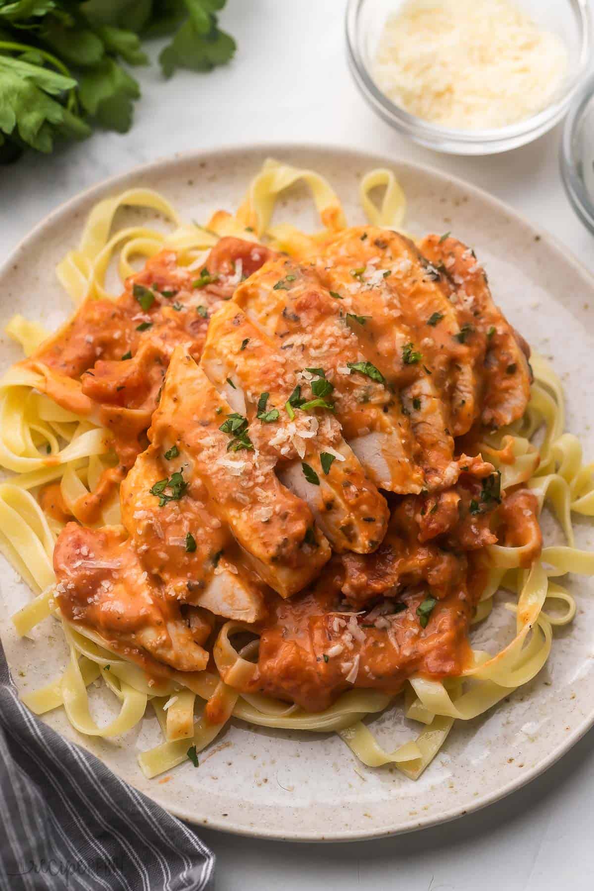 sliced tomato basil slow cooker chicken breast on a plate of pasta.
